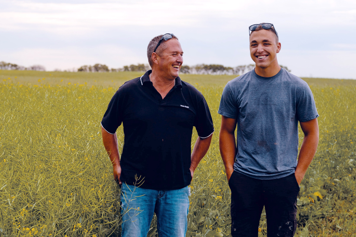 Ozeroff Family Father and Son smiling standing in front of a canola field