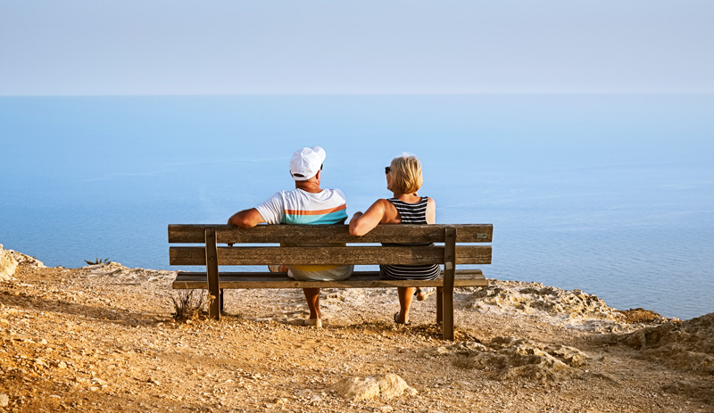 older couple relaxing on bench at seaside